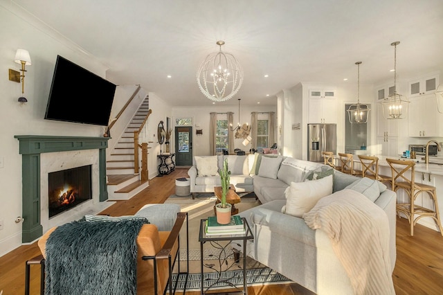 living room featuring sink, a premium fireplace, a notable chandelier, ornamental molding, and light wood-type flooring