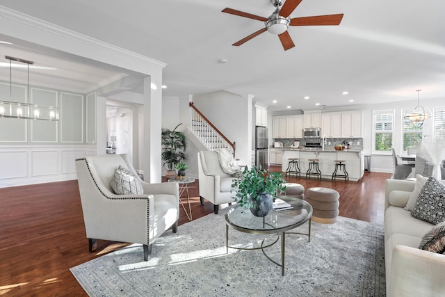 living room featuring ornamental molding, ceiling fan with notable chandelier, and dark wood-type flooring