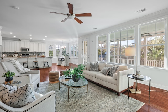 living room featuring wood-type flooring, ceiling fan with notable chandelier, and crown molding