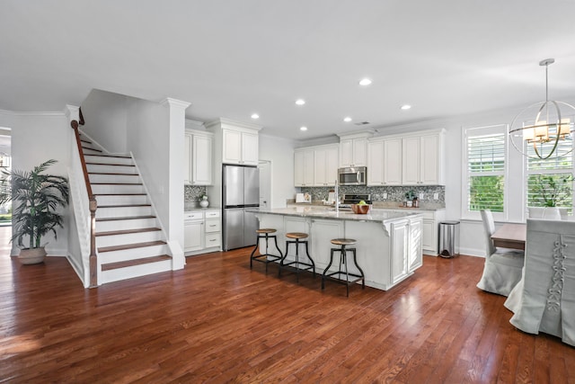 kitchen featuring a kitchen island with sink, crown molding, dark hardwood / wood-style flooring, stainless steel appliances, and white cabinets