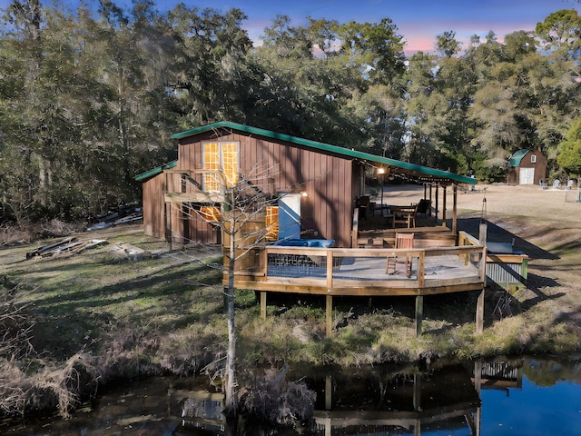 back of property at dusk with an outbuilding and a deck with water view