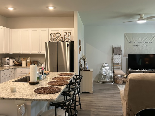 305 Camellia Bloom Dr, Moncks Corner, SC 29461 - kitchen with white cabinets, light stone countertops, a breakfast bar area, wood finished floors, and a ceiling fan