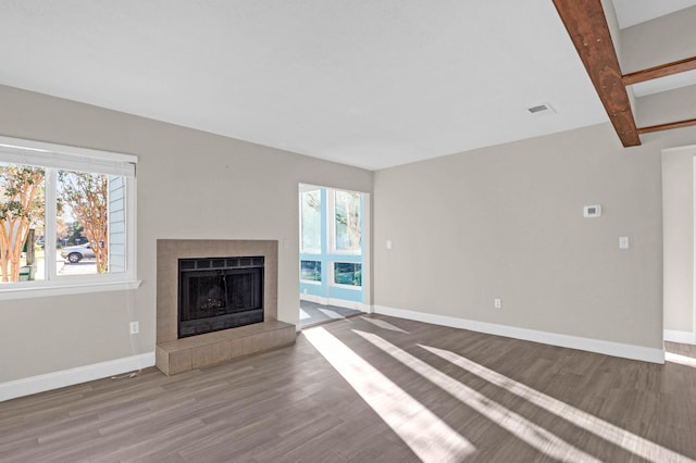 unfurnished living room featuring beam ceiling, hardwood / wood-style floors, and a tiled fireplace