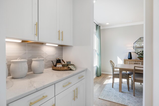 kitchen featuring light wood-type flooring, backsplash, crown molding, light stone countertops, and white cabinets