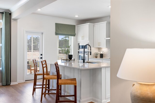 kitchen with hardwood / wood-style floors, a kitchen bar, appliances with stainless steel finishes, white cabinets, and tasteful backsplash