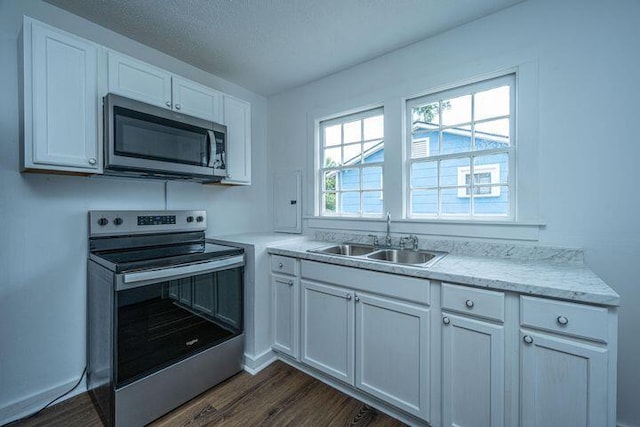 kitchen with a sink, dark wood-type flooring, appliances with stainless steel finishes, a textured ceiling, and white cabinetry