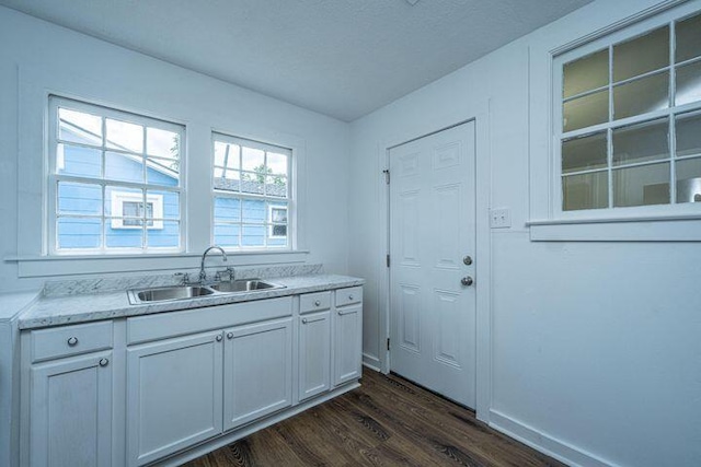 kitchen featuring baseboards, light stone counters, dark wood-style floors, white cabinets, and a sink