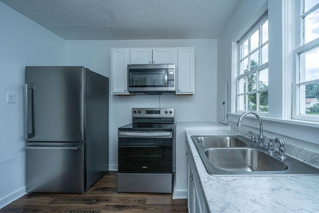 kitchen with a sink, a textured ceiling, dark wood finished floors, stainless steel appliances, and white cabinets