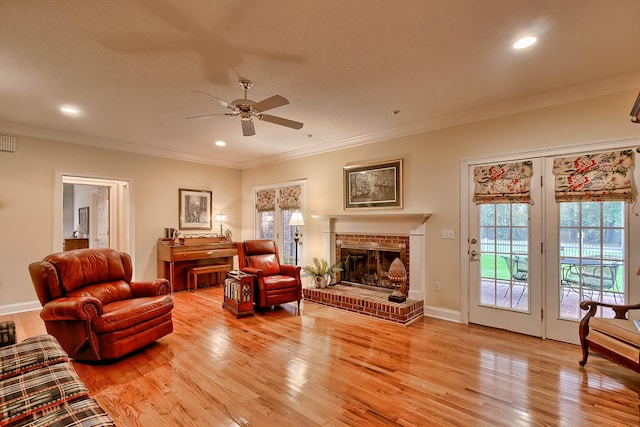 living room featuring ceiling fan, light wood-type flooring, crown molding, and a brick fireplace