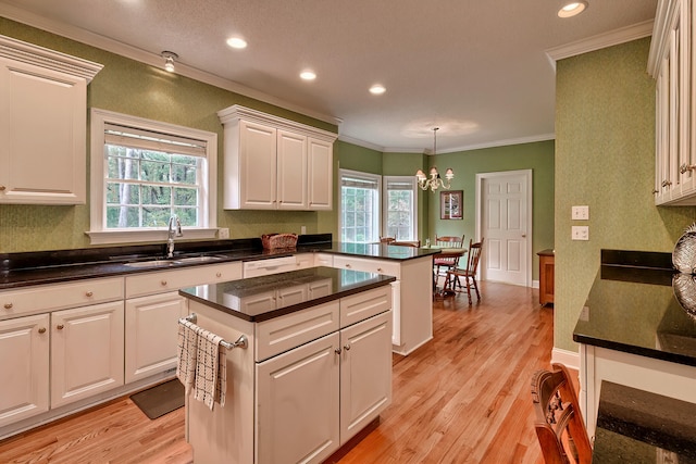 kitchen featuring white cabinetry, sink, light hardwood / wood-style flooring, pendant lighting, and ornamental molding