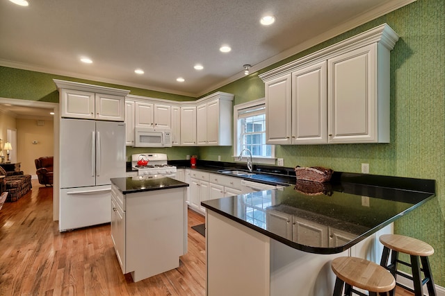 kitchen featuring a center island, white appliances, white cabinets, sink, and ornamental molding