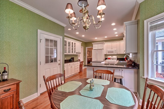 dining space with light hardwood / wood-style floors, ornamental molding, sink, and a chandelier