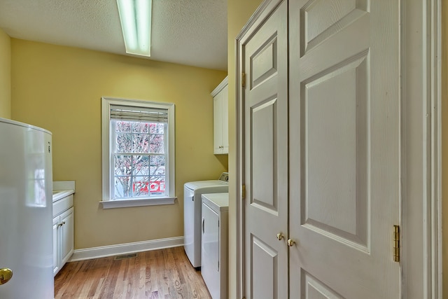 laundry area with washer and clothes dryer, cabinets, a textured ceiling, and light hardwood / wood-style flooring