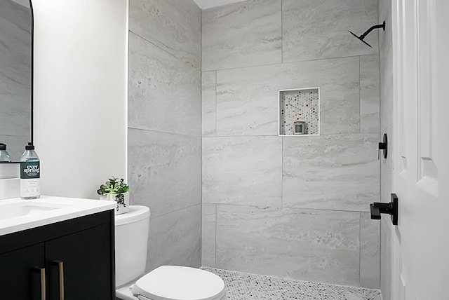 full bathroom featuring tiled shower, toilet, and vanity