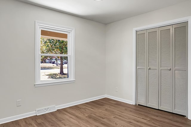 unfurnished bedroom featuring visible vents, baseboards, a closet, and wood finished floors