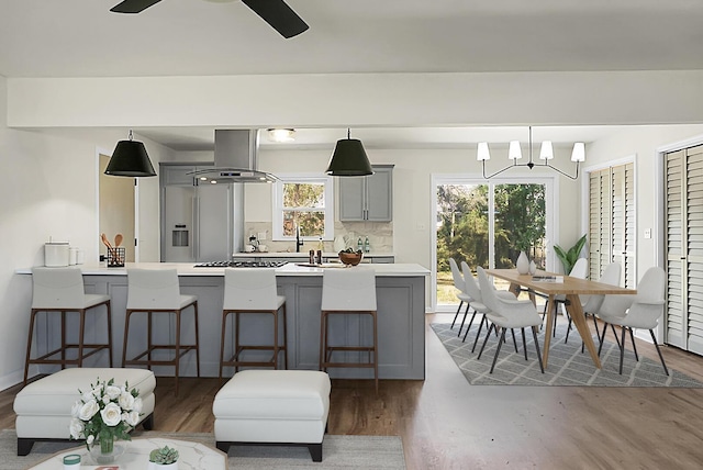 kitchen with gray cabinetry, range hood, light countertops, and a breakfast bar