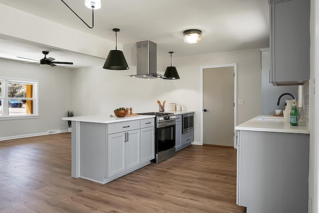 kitchen featuring gray cabinets, appliances with stainless steel finishes, wall chimney range hood, and a sink