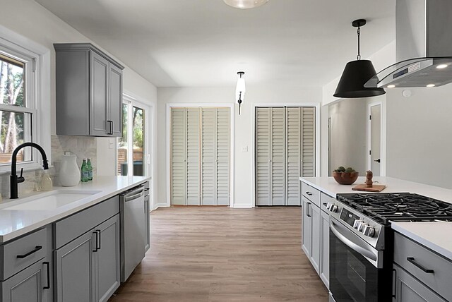 kitchen featuring gray cabinets, a sink, light wood-style floors, appliances with stainless steel finishes, and wall chimney exhaust hood