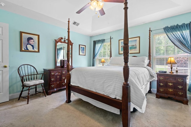 carpeted bedroom featuring a raised ceiling, ceiling fan, and visible vents