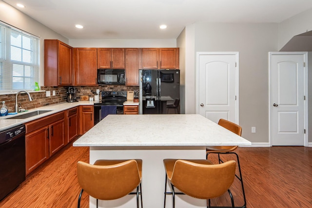 kitchen featuring a kitchen bar, sink, black appliances, and a kitchen island