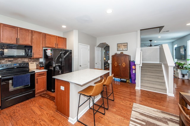 kitchen with ceiling fan, a kitchen island, black appliances, a kitchen bar, and decorative backsplash