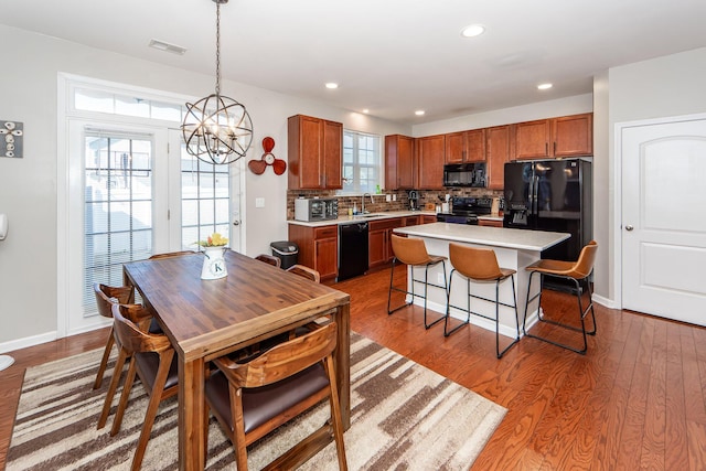 kitchen featuring a center island, tasteful backsplash, decorative light fixtures, wood-type flooring, and black appliances