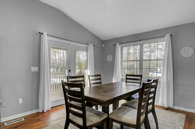 dining room with visible vents, vaulted ceiling, baseboards, and wood finished floors