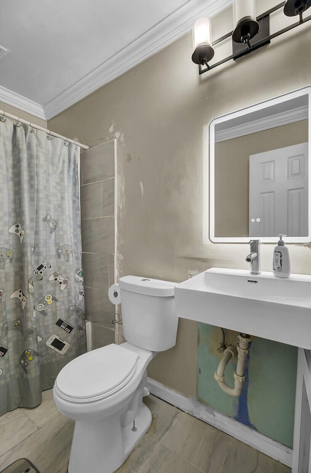 bathroom featuring baseboards, a shower with shower curtain, toilet, crown molding, and a sink