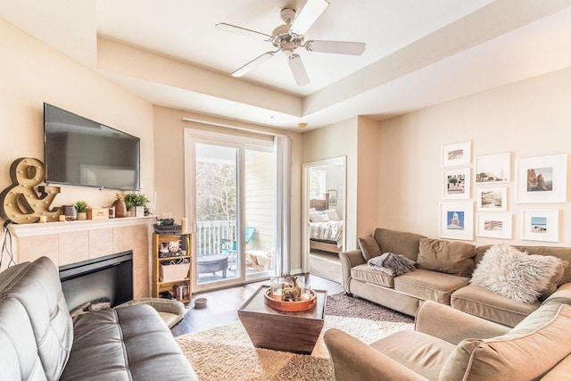 living room with ceiling fan, wood-type flooring, a tray ceiling, and a tiled fireplace