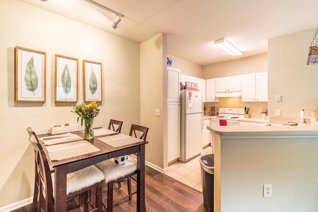 kitchen with white appliances, white cabinets, rail lighting, light wood-type flooring, and kitchen peninsula