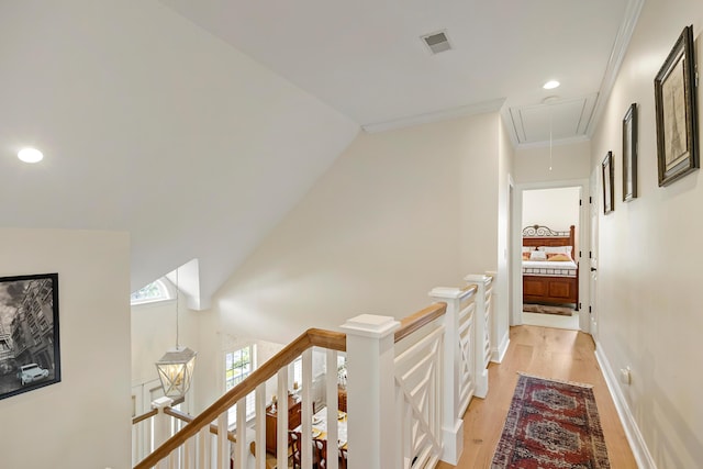hallway with visible vents, attic access, light wood-style floors, and an upstairs landing
