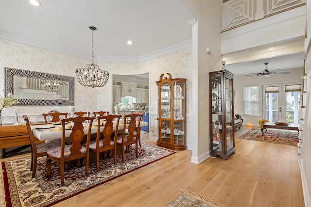 dining area featuring light wood-style floors, ceiling fan with notable chandelier, wallpapered walls, baseboards, and ornamental molding