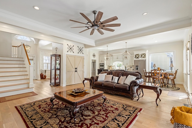 living room featuring plenty of natural light, light wood-type flooring, ceiling fan with notable chandelier, and stairs