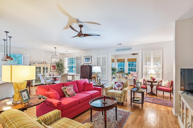 living room with ceiling fan with notable chandelier and light hardwood / wood-style flooring