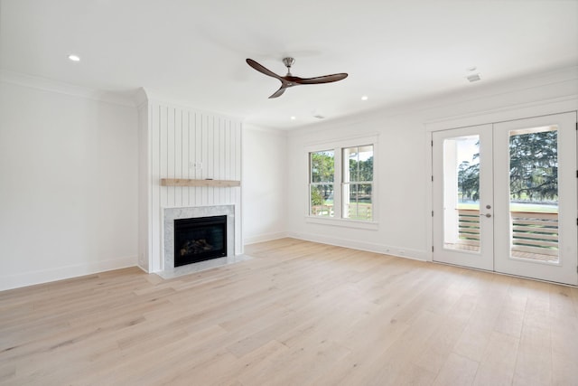 unfurnished living room with french doors, crown molding, light hardwood / wood-style flooring, ceiling fan, and a high end fireplace