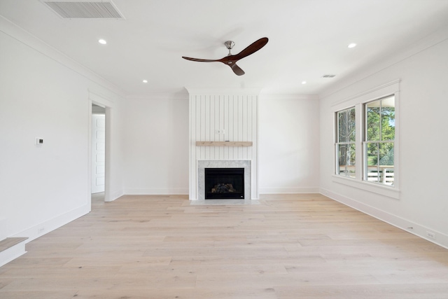 unfurnished living room featuring a premium fireplace, crown molding, ceiling fan, and light hardwood / wood-style floors