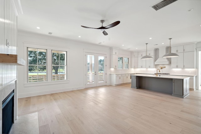 kitchen with white cabinetry, light hardwood / wood-style floors, a center island with sink, decorative light fixtures, and custom exhaust hood