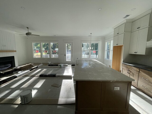 kitchen featuring a healthy amount of sunlight, a center island, hanging light fixtures, and light stone countertops