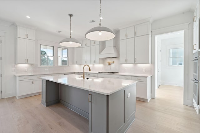 kitchen with sink, light hardwood / wood-style flooring, a kitchen island with sink, gas stovetop, and white cabinets