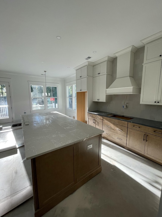 kitchen with a kitchen island, wall chimney range hood, white cabinets, and light stone counters