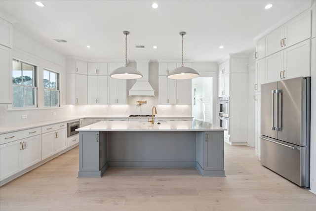 kitchen featuring white cabinets, appliances with stainless steel finishes, custom range hood, and a kitchen island with sink