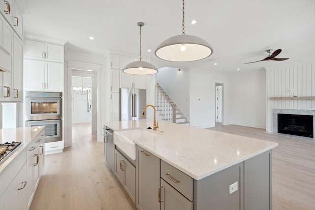 kitchen with sink, hanging light fixtures, an island with sink, stainless steel appliances, and a fireplace