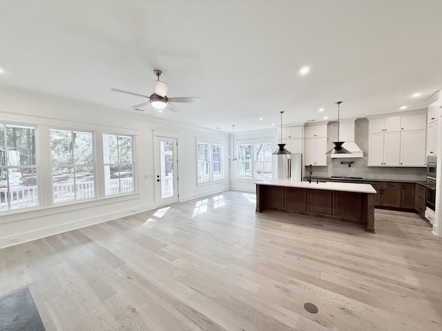 kitchen featuring wall chimney range hood, stainless steel fridge, hanging light fixtures, a center island with sink, and light wood-type flooring