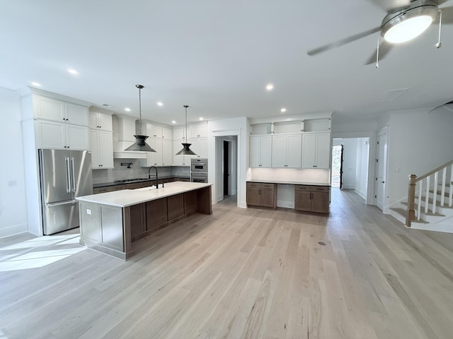 kitchen with stainless steel appliances, a spacious island, white cabinets, decorative light fixtures, and wall chimney exhaust hood