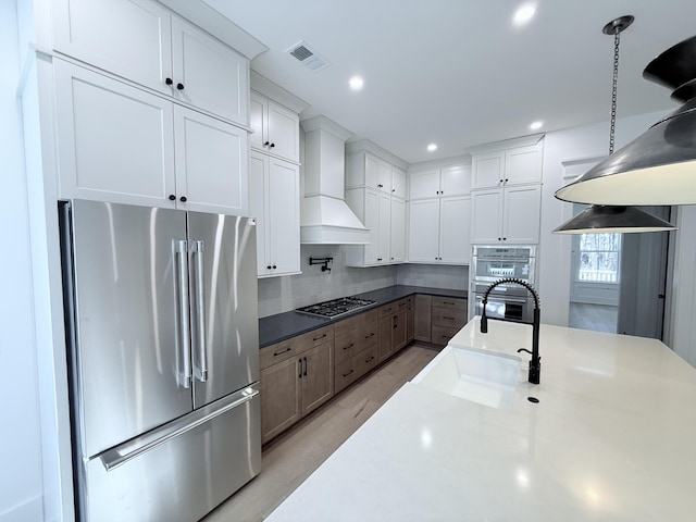 kitchen featuring sink, premium range hood, appliances with stainless steel finishes, white cabinets, and decorative light fixtures