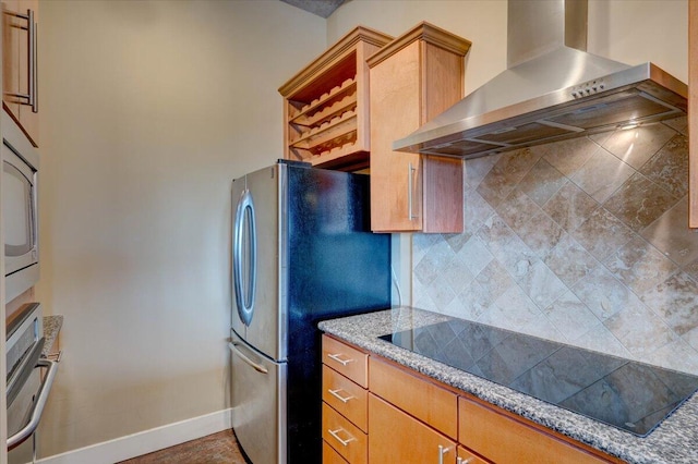 kitchen featuring stainless steel refrigerator, decorative backsplash, black electric cooktop, light stone counters, and wall chimney range hood