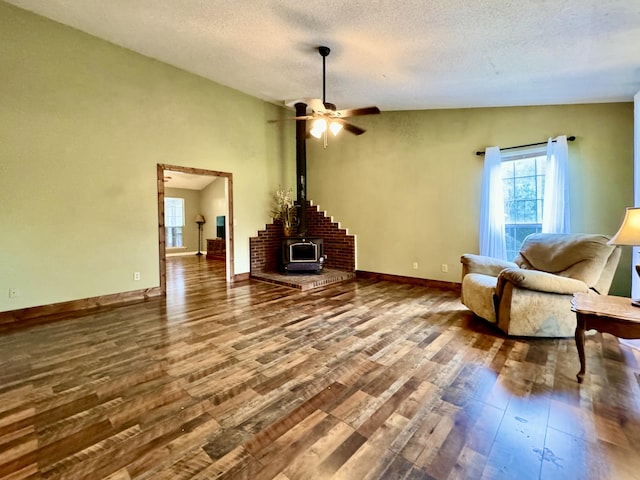 unfurnished room featuring a textured ceiling, vaulted ceiling, ceiling fan, hardwood / wood-style floors, and a wood stove