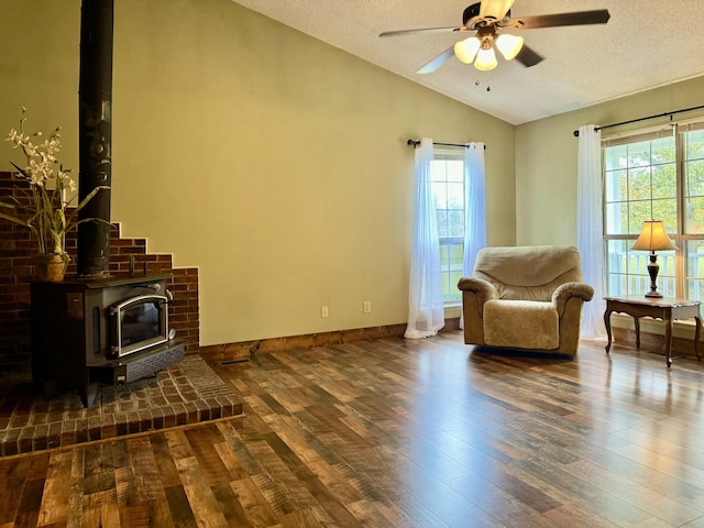 living area featuring lofted ceiling, a wood stove, ceiling fan, a textured ceiling, and dark hardwood / wood-style flooring