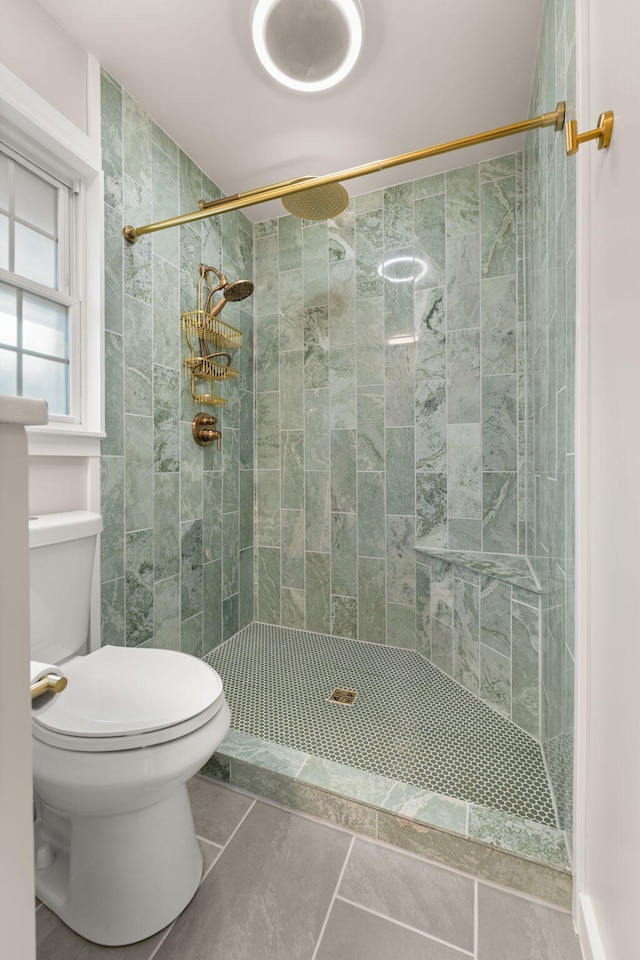 bathroom with tile patterned flooring, a tile shower, and toilet