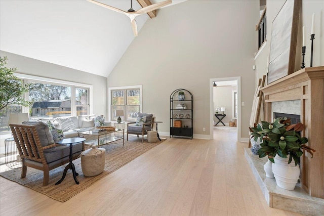 living area featuring high vaulted ceiling, light wood-type flooring, baseboards, and a premium fireplace